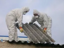 Deux opérateurs en combinaison retirant des plaques ondulées amiantées